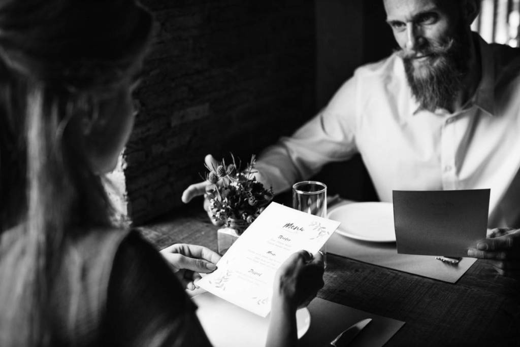 Casal sentado em uma mesa se olhando com menu na mão