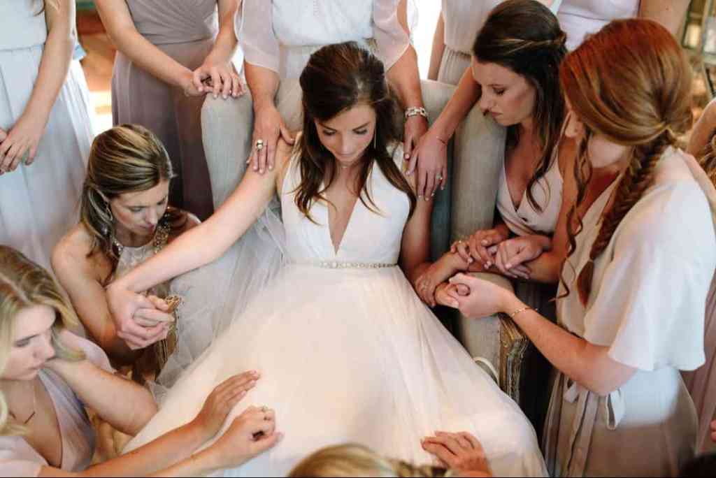 Madrinhas fazendo oração para noiva (que está sentada) antes dela entrar para o casamento