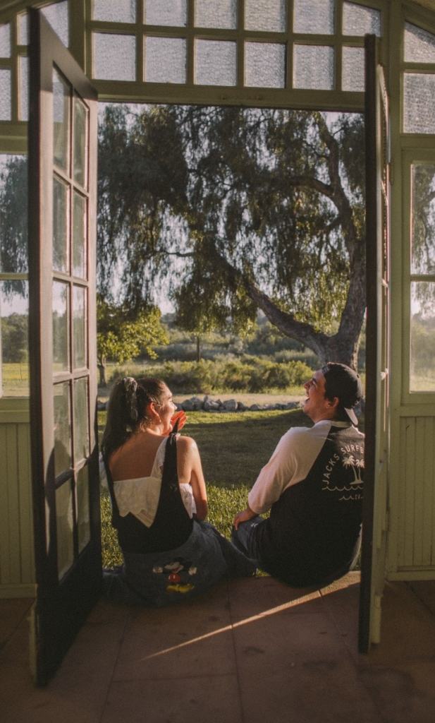 Homem e mulher sentados na porta da casa rindo