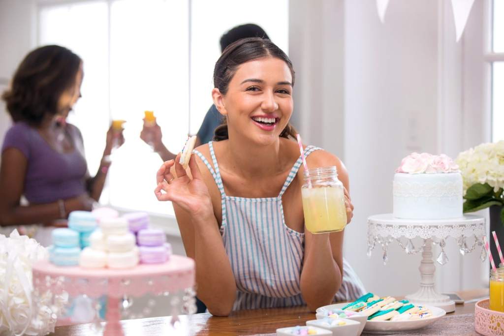 Mulher sorrindo segurando doce e suco em chá de panela - como ser a madrinha perfeita?