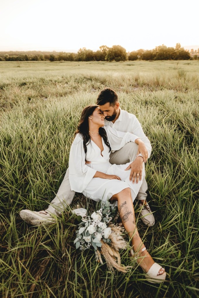 Casal com roupas brancas sentados na grama alta