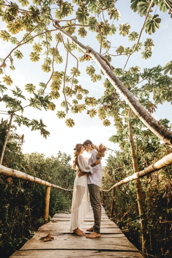 Casal abraçados quase se beijando em cima de uma ponte de madeira