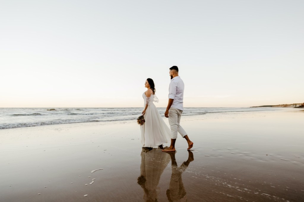 Casal de noivos descalços na praia andando