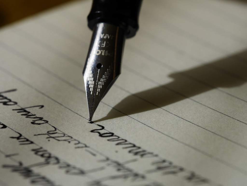 Foto focada na ponta da caneta que está escrevendo uma carta