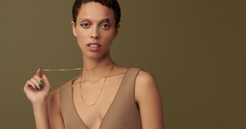 Mulher de cabelo curtinho usando vestido cor de pele e colares finos