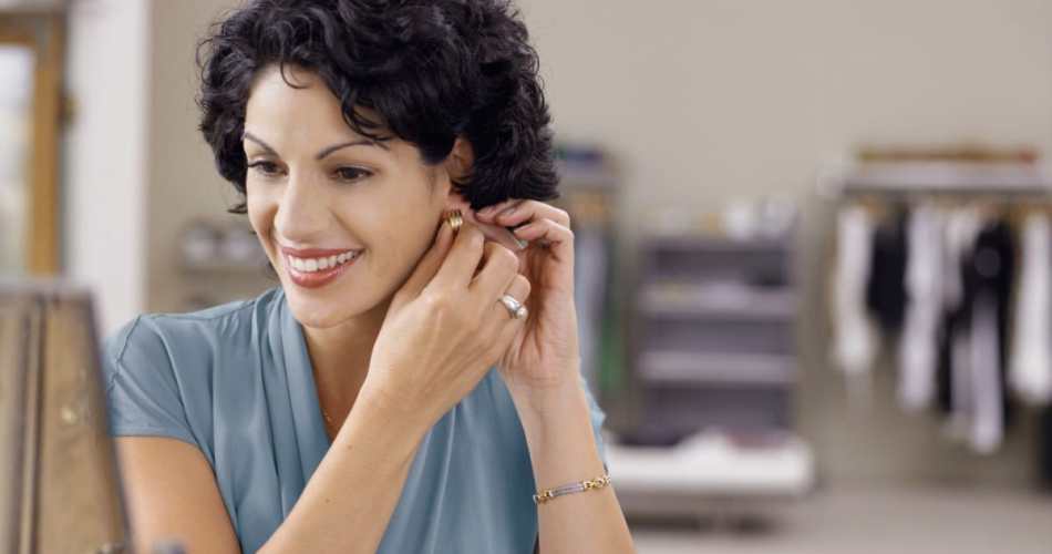 Mulher de cabelo curto cacheado sentada em sua penteadeira colocando brinco