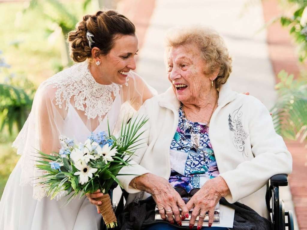 Noiva rindo com sua avó que está em uma cadeira de rodas