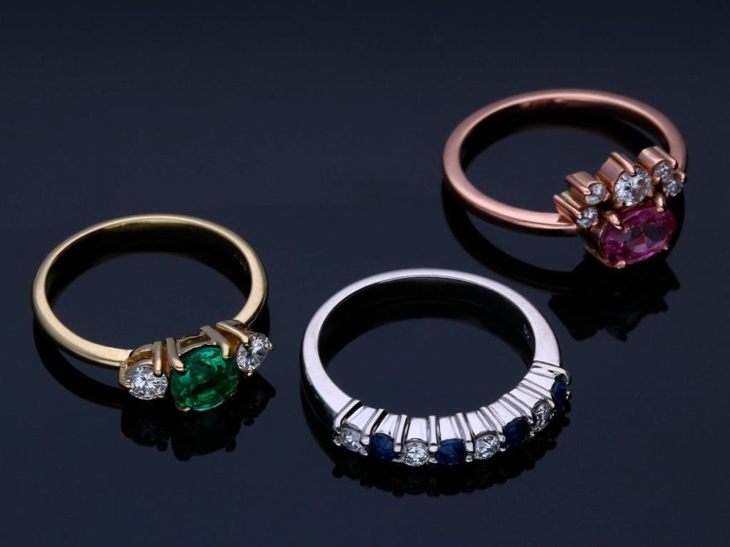 Três anéis com pedras, sendo um de ouro amarelo, um de ouro branco e um de ouro rosé;
