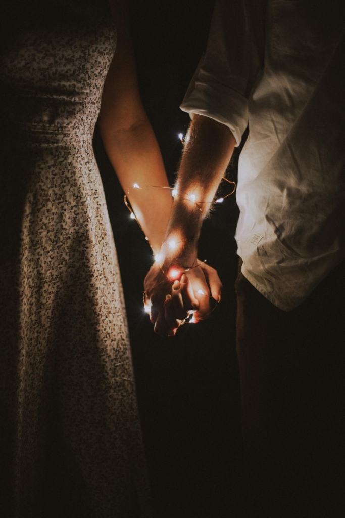 Homem e mulher de mãos dadas, em volta do braço deles tem uma luz pisca-pisca