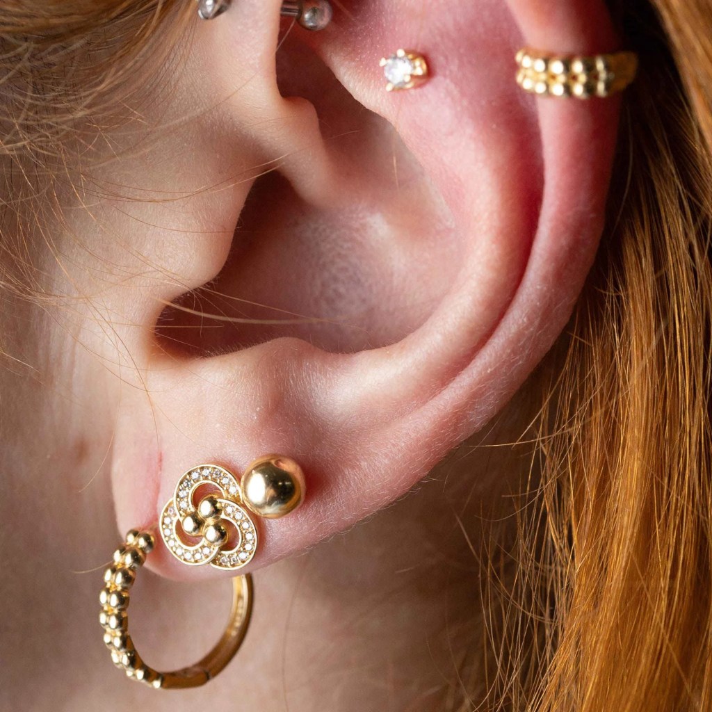 Foto de orelha com três brincos e piercings de ouro