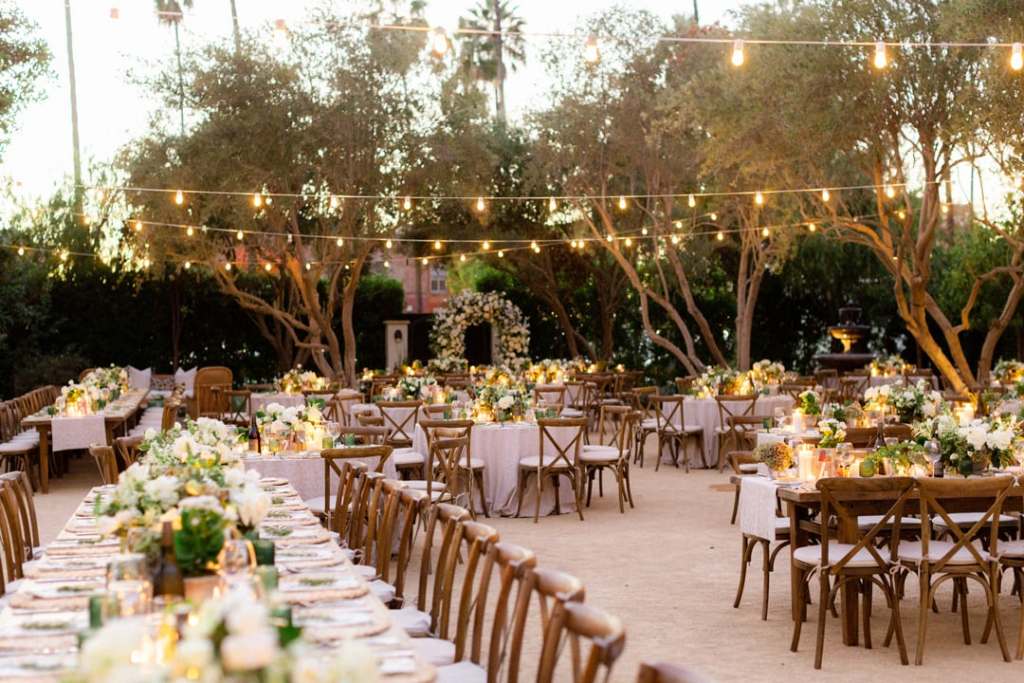Decoração de casamento ao ar livre com as mesas e cadeiras de madeira, com arranjos de flores nas mesas, e pisca pica passando por cima
