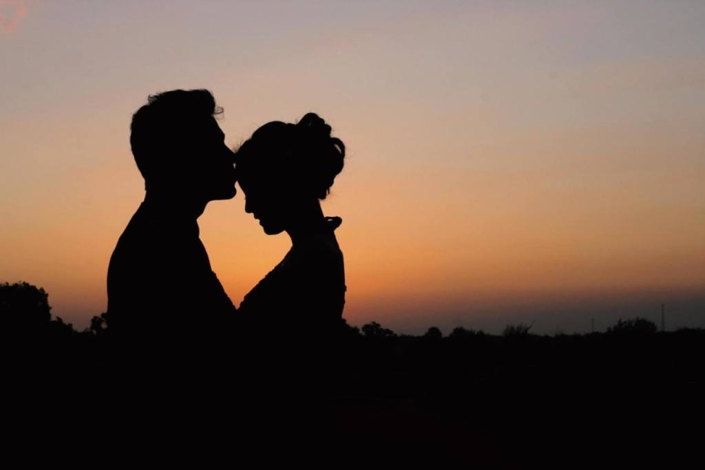 A foto mostra a sombra de um casal no por do sol, ele está beijando a testa dela - 50 legendas para foto de casal