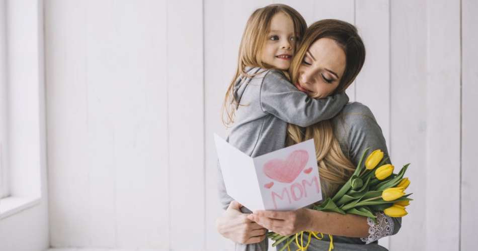 Mãe abraçada com filha que deu um cartão e flores para dia das mães