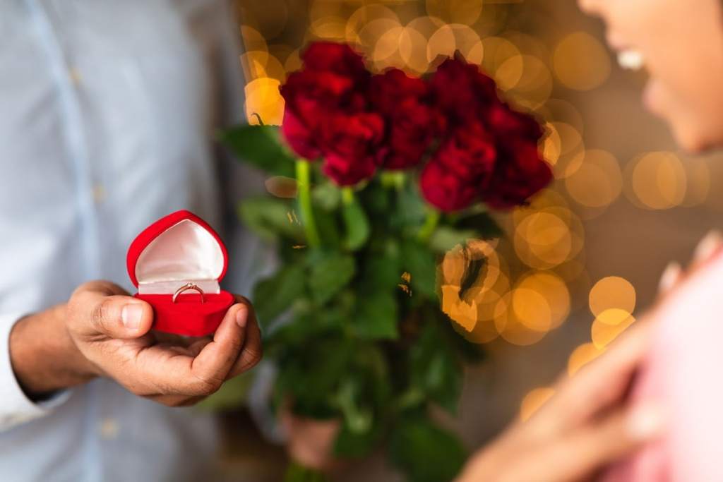 Homem segurando caixinha vermelha em formato de coração com anel de noivado