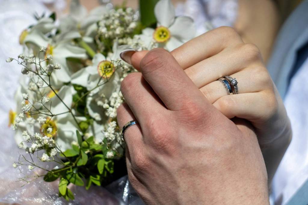 Mão de noivos usando aliança e anel de noivado em ouro branco - qual o melhor mês para casar no brasil?