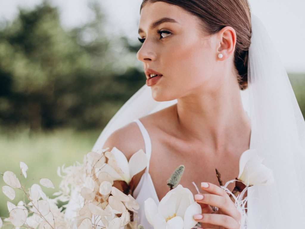 Noiva com véu e buquê em campo aberto, ela está olhando para o lado